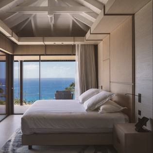 Wake up to endless ocean views from your luxurious bedroom, where exposed beams frame the stunning seascape beyond floor-to-ceiling windows.