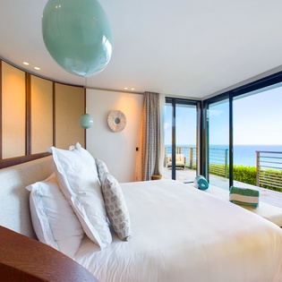Wake up to endless ocean views from your luxurious bed, where turquoise pendant lights and floor-to-ceiling windows frame the sea.