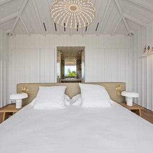Your serene bedroom sanctuary features crisp white linens, warm wood floors, and vaulted ceilings with exposed beams for ultimate relaxation.