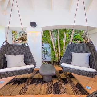 Unwind in your private hanging swing chairs, surrounded by lush tropical greenery and soft natural light filtering through every corner of this serene indoor-outdoor lounge.