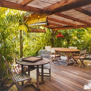 Your private tropical patio awaits, where natural wood decking and lush greenery create a serene outdoor dining sanctuary under woven shade.
