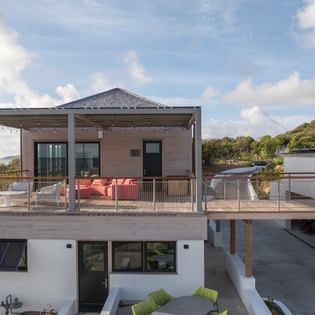 Modern coastal retreat featuring elevated deck with ocean glimpses and hillside surroundings.