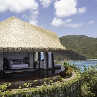 Luxury beachfront villa with thatched roof overlooking pristine bay waters and lush tropical mountains.