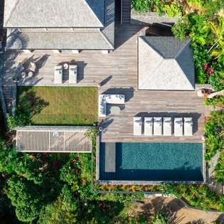 Aerial view reveals a modern tropical retreat with pristine pool, manicured gardens, and spacious outdoor terraces surrounded by lush vegetation.