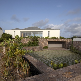 Modern architectural villa with natural stone walls and native landscaping in a serene coastal setting.