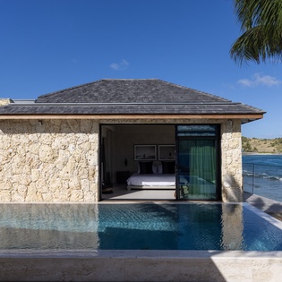 Stone villa with infinity pool overlooking turquoise waters and tropical coastline.