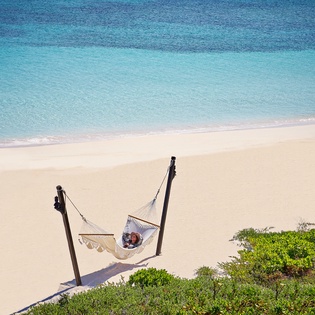 Pristine turquoise waters meet soft white sand, with lush coastal vegetation framing this tropical paradise.