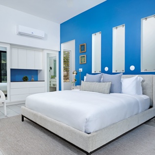 Sink into plush linens and unwind in your serene bedroom, where a vibrant blue accent wall and modern air conditioning create the perfect retreat after a day of exploring.