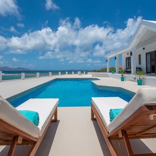A stunning rooftop retreat with pristine pool and panoramic ocean views across turquoise waters to distant mountain ranges, framed by bright Caribbean skies.