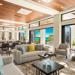 Step into your bright, open living space where warm wood ceilings and comfortable seating invite you to relax. Expansive glass doors frame stunning turquoise water views, blending indoor luxury with coastal beauty.