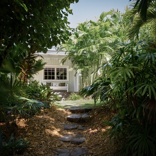 A tropical pathway winds through lush palms and greenery to this charming white cottage, creating your own private oasis.