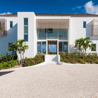 Modern tropical villa with sleek white facade and contemporary design, featuring wood accents and palm trees in pristine landscaping.