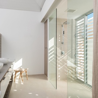 Step into your bright, modern bathroom sanctuary with a luxurious glass-enclosed shower and natural light streaming through elegant wooden blinds.