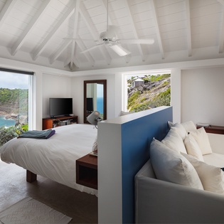 Your open-concept suite combines a plush bed with oceanfront balcony views and a cozy seating area, all beneath soaring vaulted ceilings that invite natural light and sea breezes.