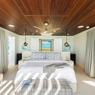 Sink into crisp linens under a stunning wood-paneled ceiling, where coastal artwork and soft natural light create your serene island retreat.