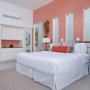 Sink into crisp linens and modern comfort in your bright, thoughtfully designed bedroom, where cool air-conditioning and elegant coral accents create your perfect retreat.