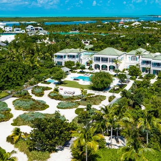 Aerial view showcasing a stunning waterfront estate surrounded by lush tropical gardens, turquoise pools, and expansive views of lagoons and coastal landscape.