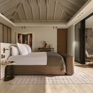 Your luxurious bedroom features soaring beamed ceilings and floor-to-ceiling windows that open to your private terrace, creating an airy sanctuary.