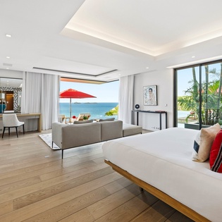 Wake up to stunning ocean views in this elegant suite with floor-to-ceiling windows and tropical scenery framing your bed.
