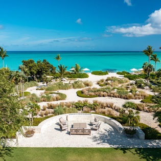 Beachfront property features direct white sand beach access, turquoise Caribbean waters, tropical landscaping with native palms and grasses, and private outdoor seating overlooking the sea.