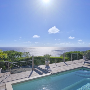 Private pool deck with stunning ocean views under brilliant blue skies and warm sunshine.