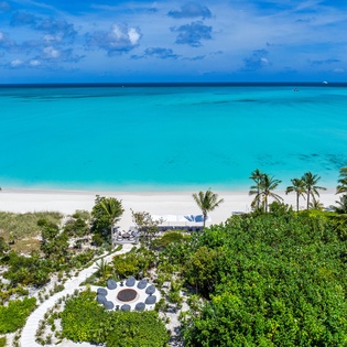 Aerial view showcasing the property nestled between lush tropical gardens and pristine turquoise waters, with white sand beach steps away.