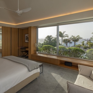 Wake up to tropical paradise through floor-to-ceiling windows. Your serene bedroom features warm wood accents and stunning views.