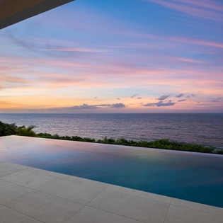 Infinity pool with stunning ocean views and colorful sunset sky creates a peaceful waterfront setting.