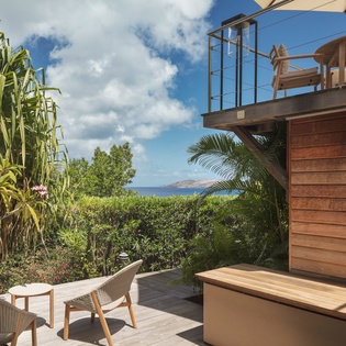 A modern wooden deck features tropical garden views and glimpses of distant coastal mountains, creating a peaceful outdoor retreat area.
