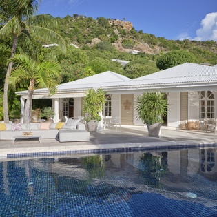 Elegant white villa nestled in lush tropical hills with pristine pool and outdoor lounging areas.