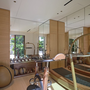 Modern gym space featuring cardio equipment, free weights, and floor-to-ceiling mirrors. Natural light filters through windows overlooking greenery, creating an energizing workout environment.