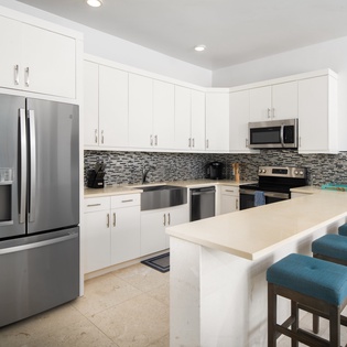 Your modern kitchen welcomes you with pristine white cabinets, stainless steel appliances, and a breakfast bar perfect for morning coffee and evening conversations.