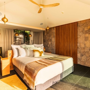 Unwind in this stylish bedroom, where natural stone walls meet mid-century warmth and your plush king bed invites restful nights under a handcrafted ceiling fan.