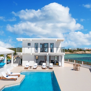 Modern beachfront villa with private pool overlooking turquoise Caribbean waters, featuring contemporary architecture and expansive outdoor living spaces perfect for island relaxation.