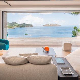 Relax in your modern living space with breathtaking ocean views stretching to distant islands through floor-to-ceiling windows.
