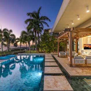 Modern luxury villa showcasing pristine pool area surrounded by tropical palms during golden hour twilight.