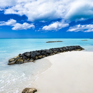 A pristine beach with powdery white sand, turquoise waters, and natural rock formations under a brilliant blue sky—ideal for peaceful seaside moments near the property.