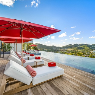 Relax on plush poolside loungers under vibrant red umbrellas while soaking in breathtaking mountain and sea views.