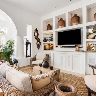 Sink into the plush sofa and unwind in this bright, airy living room. White built-ins showcase coastal treasures, while tropical plants and an archway to ocean views create your perfect beach escape.