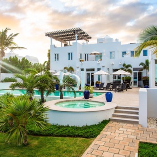 A pristine white villa nestled among swaying palms and tropical gardens, featuring an inviting pool, intimate hot tub, and peaceful outdoor lounging areas perfect for sunset relaxation.