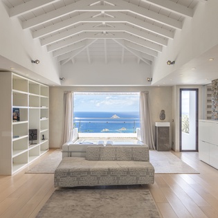 Soaring vaulted ceilings frame your stunning ocean panorama in this light-filled living space, where modern elegance meets the tranquil blues of endless sea beyond the glass.