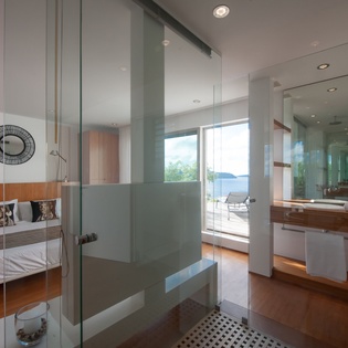 Step into your sleek glass-enclosed bathroom where modern design meets comfort, with stunning views beyond your private suite.