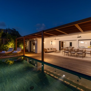 Modern luxury villa with stunning pool deck illuminated under dramatic evening sky, perfect for memorable tropical getaways.