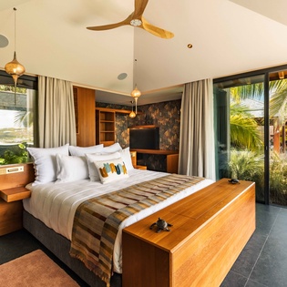 Step into your tropical sanctuary where soaring vaulted ceilings and floor-to-ceiling windows frame lush palm gardens on both sides, creating a seamless indoor-outdoor escape.