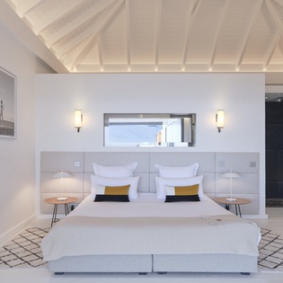 Settle into crisp white linens under soaring vaulted ceilings, where natural light and coastal charm create your serene island retreat.