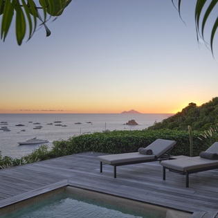 Stunning sunset views over tropical waters from this hillside deck with lounge chairs and private pool surrounded by lush palms.