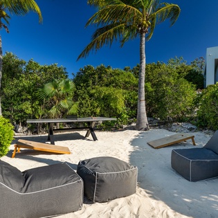 Private beachfront setting with soft sand, swaying palms, and lounge seating—your tropical escape awaits under sunny skies.