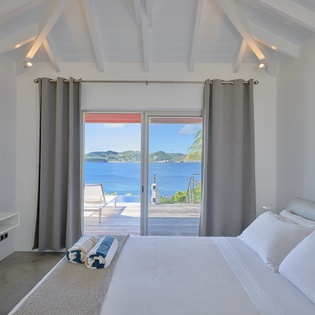 Wake up to stunning ocean views from your private bedroom, where modern comfort meets tropical elegance with exposed beams and terrace access.