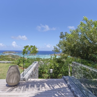Stunning tropical terrace showcasing pristine turquoise waters and lush island vegetation beyond the modern glass railings.
