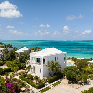Stunning oceanfront villa showcases pristine turquoise waters and lush tropical landscaping in an idyllic Caribbean setting.